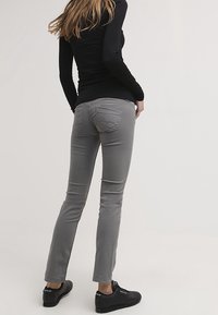 Grå slim-fit jeans med en slät textur, låg midja och bakfickor med dekorerande sömmar. Matcherade med svarta sneakers.