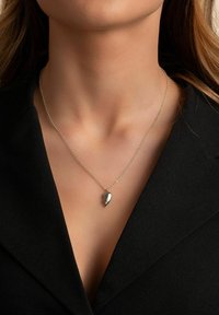 Silverfärgad kedjehalsband med en tårformad hänge med en slät yta, uppvisad mot ett svart plagg.