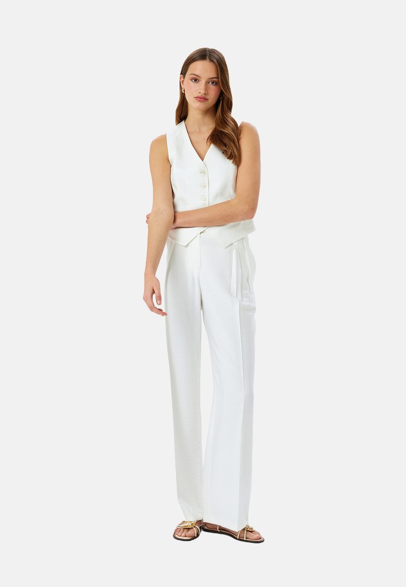 Top bianco senza maniche con bottoni, abbinato a pantaloni bianchi a gamba larga. Design semplice e texture morbida, completato da sandali color beige.