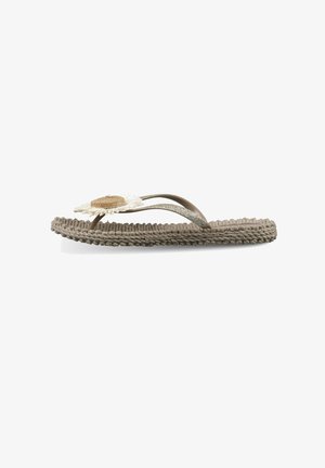 Sandalia tipo chancla plana de tejido beige con suela texturizada y decoración de flor de margarita en las correas marrones y brillantes.