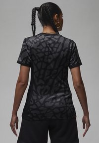 Musta urheilu paita, jossa on teksturoitu, abstrakti kuvio, lyhyet hihat ja vartalonmyötäinen siluetti, valmistettu sileästä ja kevyestä kankaasta.