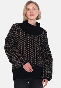 Svart stickad tröja med hög, ribbad krage och geometriskt beige mönster; lös passform med vida ärmar och ribbad nederkant.