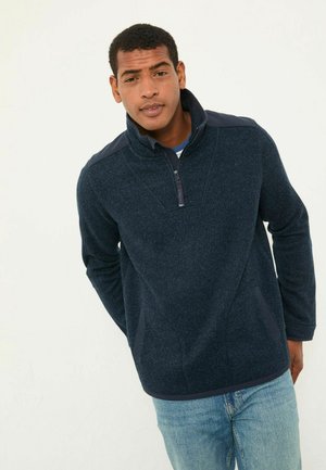 Marineblauer Fleece-Pullover mit hohem Kragen, Viertel-Reißverschluss und seitlichen Taschen. Mit kontrastierenden, strukturierten Schulterpaneelen und einer weichen, warmen Textur.