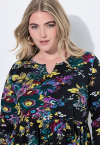 Černé květinové šaty s fialovými, žlutými a zelenými vzory. Mají výstřih ve tvaru klíčové dírky a nařasený pas pro pohodlný střih.
