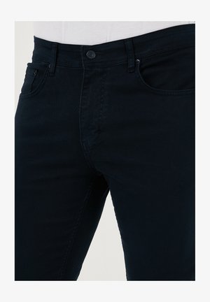 Jeans blu scuro in denim di cotone. Presentano un design classico con chiusura a bottone, due tasche frontali e una texture liscia.