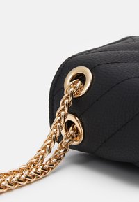 Czarna, teksturowana skórzana torba z pikowanym wzorem, z paskami z złotego łańcucha przewleczonymi przez złote metalowe oczka.