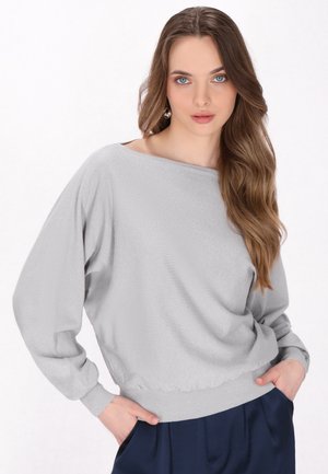 Pull gris clair avec une texture douce, encolure large bateau et poignets côtelés ; ourlet ajusté ; porté avec un pantalon bleu marine.