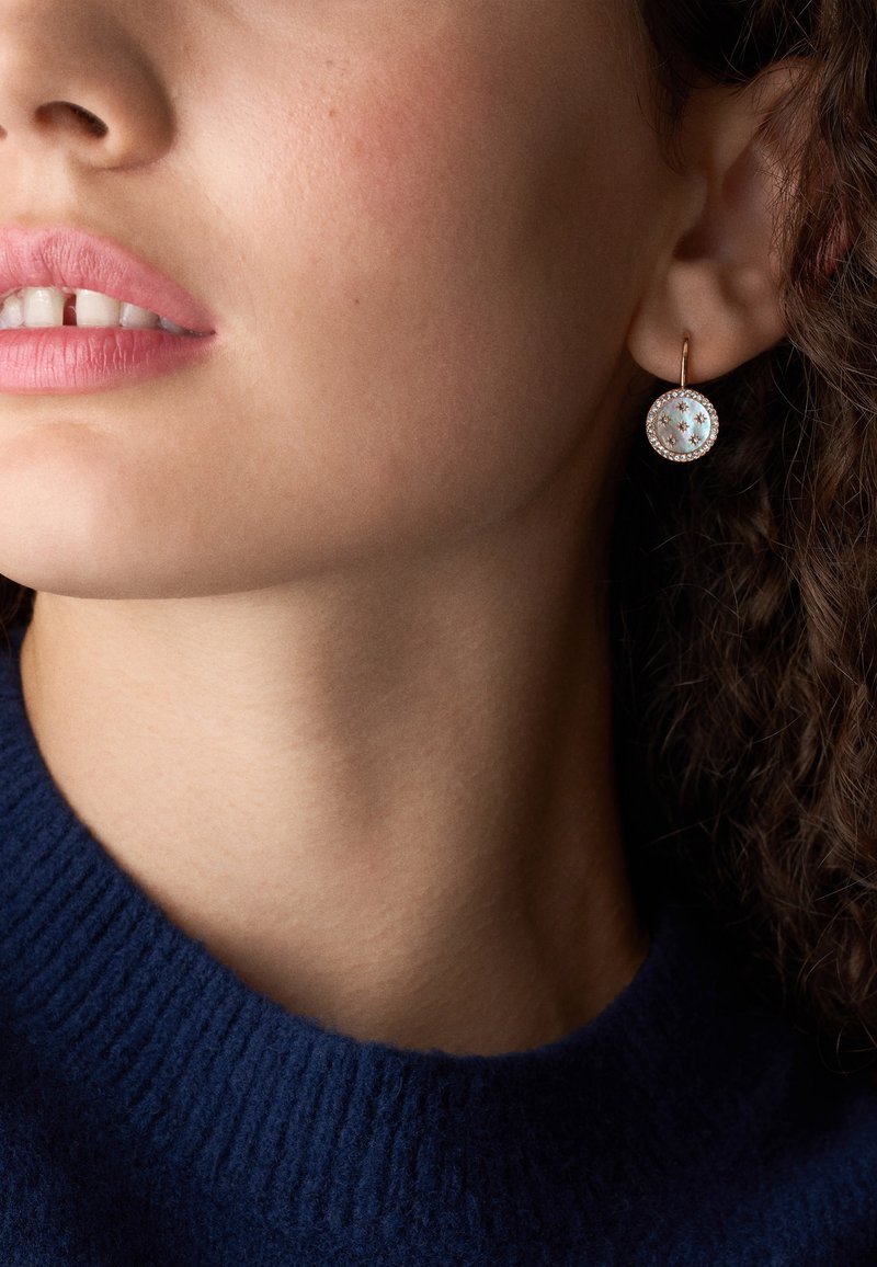 Gli orecchini a cerchio in oro rosa presentano un design circolare con un centro bianco e iridescente e piccoli diamanti chiari circostanti, appesi a un gancio semplice.