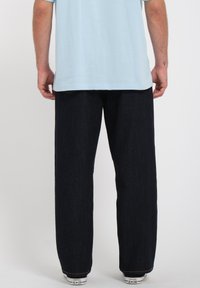 Vaqueros de mezclilla azul oscuro con un diseño de pierna recta, detalles de costura visibles y acentos de bolsillo en contraste, combinados con zapatillas blancas.
