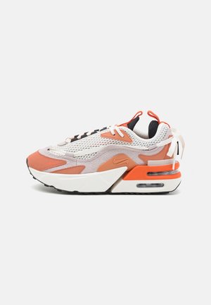 Lavtsiddende sneaker med hvidt mesh, lyse orange og beige ruskindsoverlejringer, hvide snørebånd og synlig luftpolstring i den orange og hvide sål.