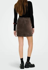 Gonna marrone in velluto a coste con vita elastica, lunghezza corta e trama a coste verticali. Indossata con scarpe nere oversize e calzini di pizzo.