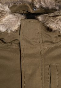 Zielona parka z futrzanym obszyciem kaptura, z plisą, przeszyciami i boczną kieszenią. Gładka faktura tkaniny.