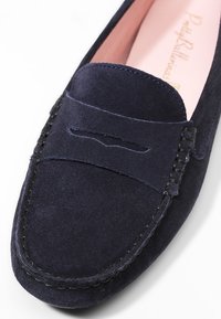 Mocassin en daim bleu marine avec un détail cousu et une petite découpe sur le devant. Surface texturée et doublure rose pastel.