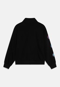 Sweatshirt noir avec un col montant, des poignets côtelés et des détails au dos. La manche gauche présente des motifs circulaires colorés. Texture de tissu douce.