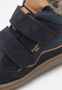 Marineblå semsket og nett joggesko med doble borrelåsremmer, brune lærdetaljer, sømdetaljer og en strukturert gummisåle.