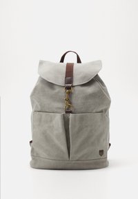 Sac à dos en toile grise avec rabat pliant, sangle marron, fermoir en métal et deux poches avant. Tissu texturé avec une forme rectangulaire.