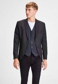Black tailored blazer over a navy waistcoat, featuring a notch lapel, single chest pocket, long sleeves, and buttoned front.