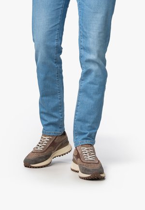 Baskets en maille et en daim marron avec des lacets crème, des semelles en caoutchouc et un motif supérieur texturé, accompagnées de jeans bleu clair.