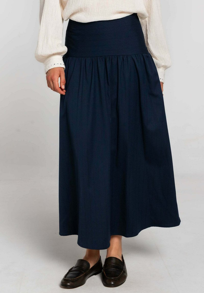 Falda de cintura alta en azul marino, hecha de una tela ligera, con un diseño plisado y una textura suave, combinada con mocasines marrón oscuro.