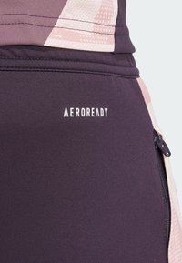 Leggings de sport en tissu violet foncé avec un motif géométrique rose clair. Présente une fermeture éclair noire et un logo "AEROREADY" en blanc.
