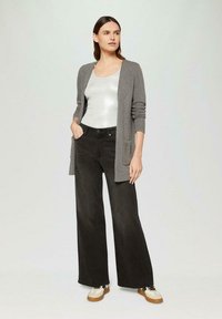 Gray long cardigan over a silver tank top, paired with wide-leg black jeans and white sneakers with brown soles.