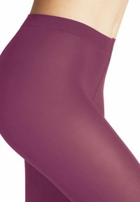 Ingrandimento di una persona che indossa leggings aderenti viola a vita alta, con in evidenza l'area laterale e dell'anca su uno sfondo bianco.