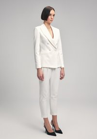 White double-breasted blazer with notched lapels, paired with white cropped trousers and black high-heeled shoes, featuring a smooth texture.