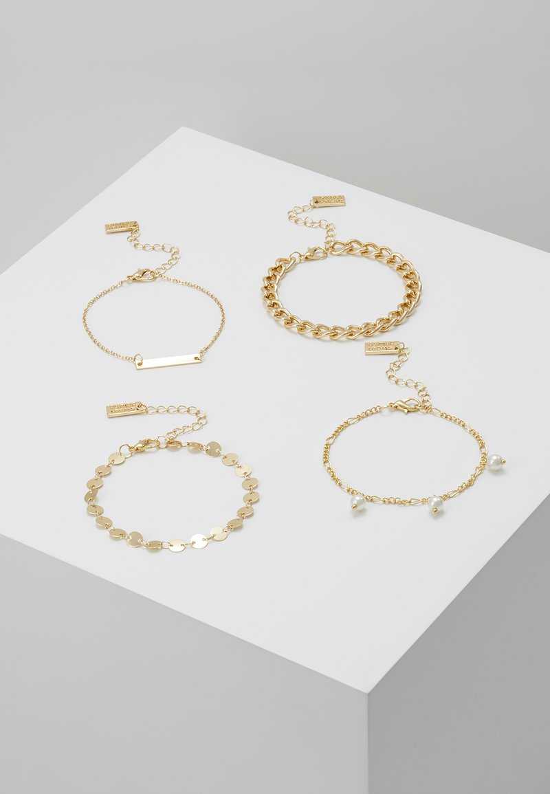 Keturi auksiniai apyrankės, išdėstytos ant baltos paviršiaus: viena grandinėlė, viena plokščia vardinė plokštelė, viena diskų grandinėlė ir viena apyrankė su perlų akcentais.