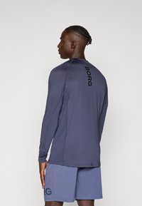 Langærmet atletisk skjorte i mørkeblå med kontrasterende sort "BORG" logo på ryggen. Glat, strækbart materiale, parret med lyseblå shorts.