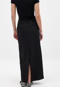 Zwarte maxi rok met een achterkant split, voorzien van een aansluitende tailleband en zijzakken. Gepaard met zwart-wit gestreepte schoenen.