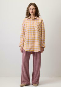 Sárga és levendula színű, kockás flaneling, elől zsebbel, párosítva széles szárú, texturált rózsaszín kordbársony nadrággal és bézs slip-on cipővel.