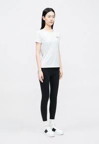 Rövid ujjú, fehér sport póló fekete leggingssel és fekete részletekkel díszített fehér tornacipővel párosítva. Sima anyagból, testhezálló kialakítással.