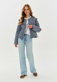 Kurtka puchowa w kratę w kolorze granatowym i białym, z falbanami. Połączona z jasnoniebieskimi dżinsami z rozszerzanymi nogawkami i szpilkami w leopardzi wzór.