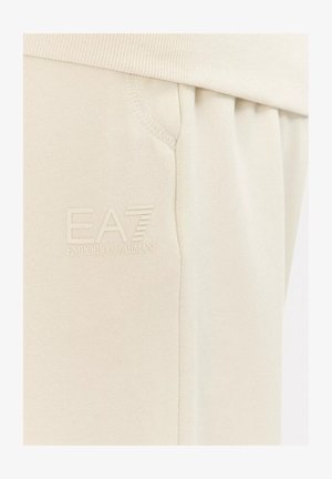 Pantaloni della tuta beige realizzati in tessuto morbido, con vita a coste, tasche laterali e logo EA7 in rilievo sotto la linea della vita.