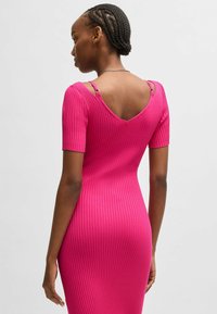 Dopasowana różowa sukienka prążkowana z krótkimi rękawami i wycięciem w kształcie litery V z tyłu. Posiada małe metalowe akcenty na ramiączkach oraz gładką fakturę.