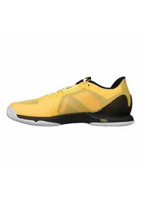 Zapatilla deportiva amarilla con parte superior de malla, talón negro y suela blanca. Presenta un diseño aerodinámico con ventilación estratégica y detalles texturizados.