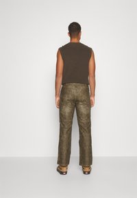 Brun ärmlös topp i strukturerad tyg, kombinerad med olivgröna, något glansiga byxor med vida ben som har fickor och en slät yta.