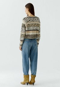 Strickpullover mit Tierdruckmustern in Beige- und Brauntönen, kombiniert mit lockeren hellblauen Jeans und gelben Leder-Ankle-Boots.