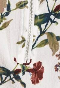 Tessuto con zip a fiori, con uno sfondo bianco e motivi floreali multicolori in rosso, verde e marrone; superficie testurizzata.