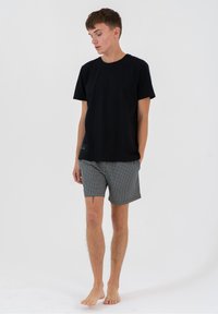 Czarny bawełniany t-shirt i szare kratkowane szorty kąpielowe. Szorty mają sznurek w pasie i małą metkę z boku. Na bose stopy.