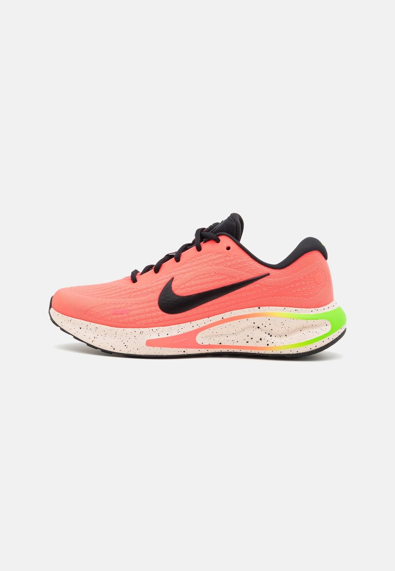 Chaussure de course corail vif avec le logo Nike noir, lacets noirs, semelle intermédiaire blanche tachetée et accent vert néon au talon.