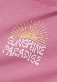 Różowa bluza z grafiką, na której widnieje napis "SŁONECZNY RAJ" oraz żółte promienie słońca. Miękki materiał o gładkiej teksturze.