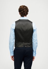 Schwarze Satinweste mit glatter Oberfläche, verstellbarer Riemen hinten, getragen über einem hellblauen Hemd, kombiniert mit dunklen Hosen.