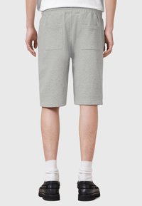 Grijze katoenen shorts met een trekkoord in de taille, twee achterzakken en een knielange snit. Draagt zwarte schoenen en witte crew-sokken.