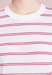 Weißes Baumwoll-T-Shirt mit roten horizontalen Streifen, rundem Halsausschnitt und weicher Textur. Keine zusätzlichen Verzierungen oder Muster.