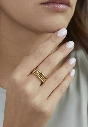 Goldener Ringstapel mit drei Ringen: ein glatter, ein mit einem Drehmuster strukturierter und ein mit kleinen klaren Steinen verzierter Ring.