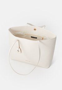 White faux leather tote bag with long handles, a gold snap closure, and an interior zip pocket. Features a logo tag on the side.