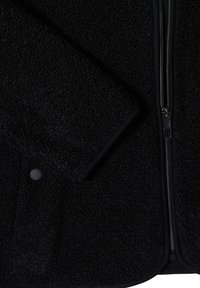Veste polaire noire texturée avec une manche visible, une fermeture éclair et un bouton-pression sur une poche.