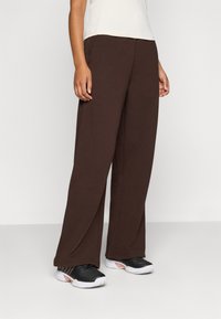 Brown wide-leg pants made of soft fabric, featuring a smooth texture and a relaxed fit, paired with black athletic shoes.