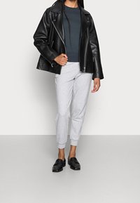Black leather biker jacket with zippers; dark gray fitted sweater; light gray jogger pants; black loafers. Minimalist, casual outfit.